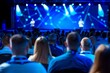 Focused audience at a professional conference event engaging with a presenter delivering a speech on stage with vivid lighting.