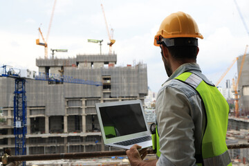 A project engineer at a construction site holds a laptop to track progress according to the plan. Monitoring progress is key to success. Our project engineer is on-site, armed with a laptop to ensure 