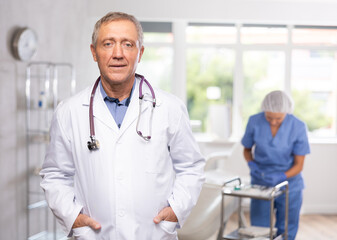 smiling aged man dermatologist standing in light cosmetology cabinet with wide windows