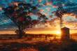 Colorful Australian outback sunset landscape with a windmill, water tank and gumtrees and a firey sky with clouds with a sunburst and lens flare.