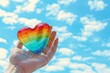 Hand holding rainbow heart shape symbol for pride month against blue sky background Generative AI
