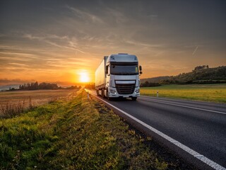 Wall Mural - white truck driving on the asphalt road in rural landscape at sunset