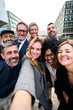 © CarlosBarquero - Vertical selfie of a cheerful team of diverse business people in formal suit looking smiling at camera gathered outside the work building. Positive emotion team work celebrating success together