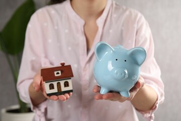 Wall Mural - Woman with house model and piggy bank indoors, selective focus