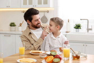 Poster - Father and his cute little son having fun during breakfast at table in kitchen