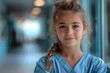 Young girl with a braided hairstyle, wearing blue medical scrubs, smiles confidently in a bright hospital corridor