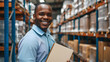 A man in a vest is smiling and holding a piece of paper. He is standing in a warehouse with shelves full of boxes