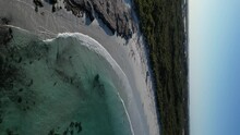 Slow-motion of vehicle driving along Wylie Bay Rock beach, Esperance area in Western Australia. Aerial drone and vertical format. Sky for copy space