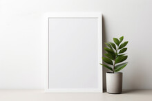A White Picture Frame Hangs On A White Wall With A Potted Plant On The Floor In Side Of It.