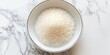 Bowl of white granulated sugar on a marble background, baking ingredient.