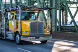 Fototapeta Mapy - Yellow classic bonnet big rig semi truck tractor with empty two level hydraulic semi trailer driving on the truss arched bridge