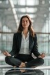 © Ilia - Businesswoman in a suit sits on office desk in a lotus yoga pose, meditating. The concept of stress reduction and anxiety relief at work.