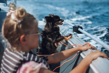 A Girl And A Dog Enjoying A Boat Ride On A Glorious Summer Day, Both Holding The Rail And Looking Out Over The Ocean.