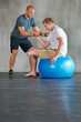 © peopleimages.com - Physical therapy, balance and exercise ball with a man with a disability and physio consultation for rehabilitation. Physiotherapy, help and workout for health with helping and wellness for mobility