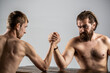 © Yevhen - Arms wrestling thin hand, big strong arm in studio. Two man's hands clasped arm wrestling, strong and weak, unequal match. Heavily muscled bearded man arm wrestling a puny weak man