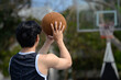 Back view of young basketball player throwing the ball to the basket at outdoor court