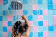 kid rinsing hair under a showerhead with blue and pink tiles