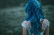 Rear view of a woman with vibrant blue hair and lace dress in a moody natural setting. Fantasy and mystery concept for design and print with a focus on hairstyle