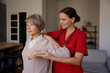 Woman rehabilitation therapist assisting senior female exercising at home
