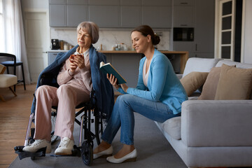 Smiling adult daughter reading for old mother with mental disorder