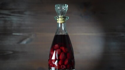 Wall Mural - Glass bottle of  homemade red raspberry liqueur on a wooden background, rotates, close up. Berry alcoholic drinks concept