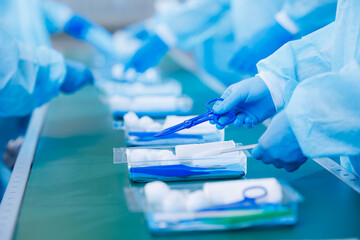 Surgery kit on conveyor line, closeup of medical staff gloved hands sorting blue med instrument scissors, tool of doctor pharmacy, clear light toning