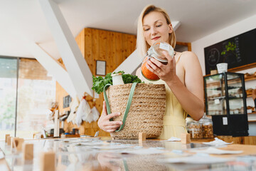 Wall Mural - Smiling woman with glass jar of red lentils in zero waste shop. Female customer with basket of organic products in modern plastic free store.