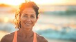 Smiling woman with curly hair wearing orange tank top standing on beach with ocean in background during sunset.