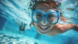 A joyful underwater scene with a person wearing blue goggles smiling broadly and swimming in clear blue water with another swimmer in the background.