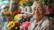 © iuricazac - An elderly man with glasses wearing a striped shirt sitting in front of a colorful flower display with a warm smile on his face.