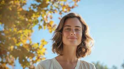 Wall Mural - A woman with a radiant smile looking directly at the camera set against a backdrop of a clear blue sky and autumnal foliage.