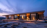 Fototapeta  - A modern minimalistic style single story house has a flat roof, clean lines, and large glass windows that emit warm light, contrasting with the cool dusk light