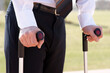 A man in formal wear, with a blazer and suit trousers, is using crutches