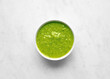 Bowl of basil pesto top view on white marble background top view, green vegetable sauce