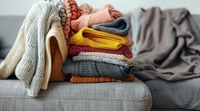 Bunch Of Unfolded Sweaters Prepared For Sorting. A Messy Pile Of Knitwear Lying On Grey Textile Sofa