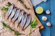 Fresh horse mackerel fish top view on paper and wooden blue background, mushrooms, greens and lime are laid out next to it