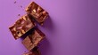 Chunks of chocolate with nuts on a purple background, one piece is broken in half revealing the interior.