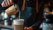 Barista pouring milk into a coffee cup, creating creamy beverage, with blurred background.