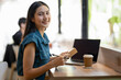 © Wasana - Smiling young woman engrossed in writing notes in a notebook in a café with a takeaway coffee cup on the table.