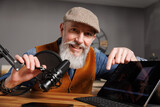 Fototapeta  - Studio podcast avec un micro et un ordinateur tablette et un homme souriant au look stylé et vintage avec une barbe hipster