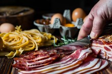 closeup of a hand slicing cured meat with eggs and pasta in the background