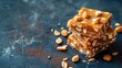 © Татьяна Макарова - Stacked peanut brittle pieces on a blue textured background with scattered nuts and caramel shards.