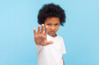 © khosrork - Portrait of serious strict little boy with curly hair showing stop gesture reaching palm to camera forbidden behavior in school. Indoor studio shot isolated on blue background.