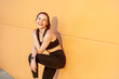 © khosrork - Portrait of good looking pleased friendly woman wearing black sportswear finishing her workout expressing happiness enjoying active healthy lifestyle. Outdoor shot against orange wall.