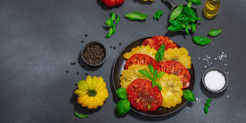 Colorful Heirloom tomato harvest. Ripe ribbed vegetables with fresh basil leaves. Wooden background