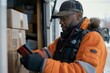 A delivery driver in an orange jacket is looking at a box, scanning it for delivery using a handheld device