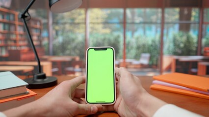 Mobile phone with green screen in hands of man in background of library. Advertising area, workspace mock up.