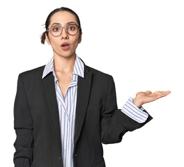 Confident young Caucasian businesswoman on studio background impressed holding copy space on palm.