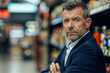 Portrait of mature businessman standing in aisle of supermarket and looking at camera
