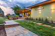 A contemporary home exterior captured in the soft light of early evening, featuring soothing sage green walls. Vibrant grass, brick, stone, and meticulous landscaping frame the inviting space.